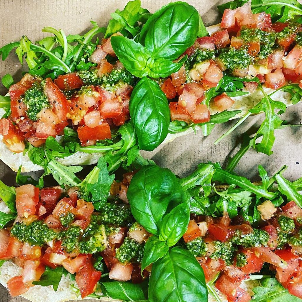 Brusschetta wird hier gezeigt. Es setzt sich aus Ofenbrot, Tomaten, Rucola, Pesto und Basilikum zusammen