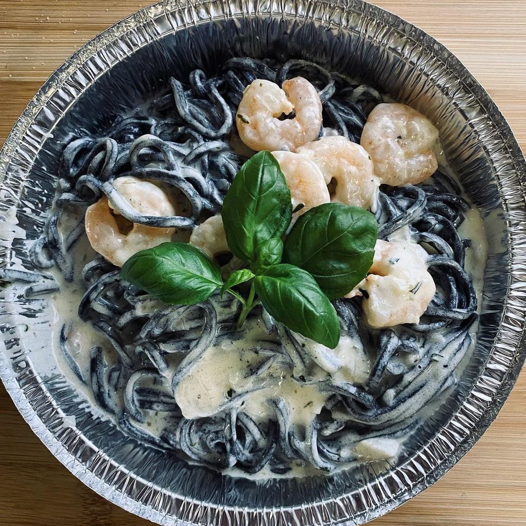 Hier sieht man Fettuccine Nero. Das Gericht enthält schwarze Bandnudeln mit Garnelen, umgeben von einer Sahnesoße